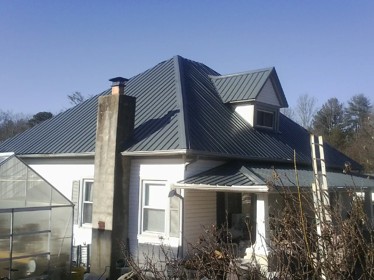 Dark blue standing seam metal roof on a white farmhouse with dormer — Slate & Tile Roof Repair by Roofing Brothers in Red Cloud