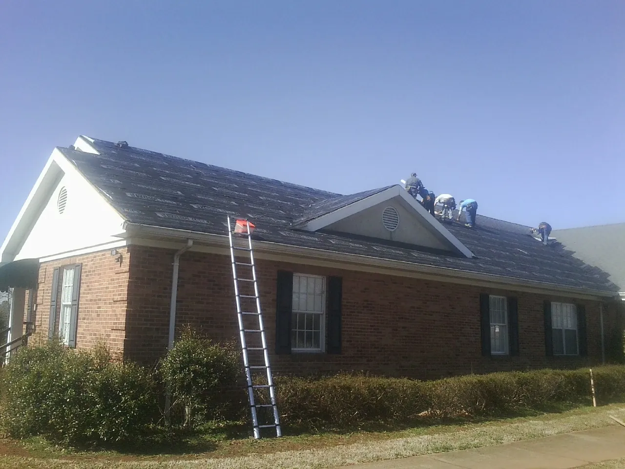 Crew tearing shingles off a brick ranch roof with a ladder set — Metal Roof Repair work by our crew in Red Cloud