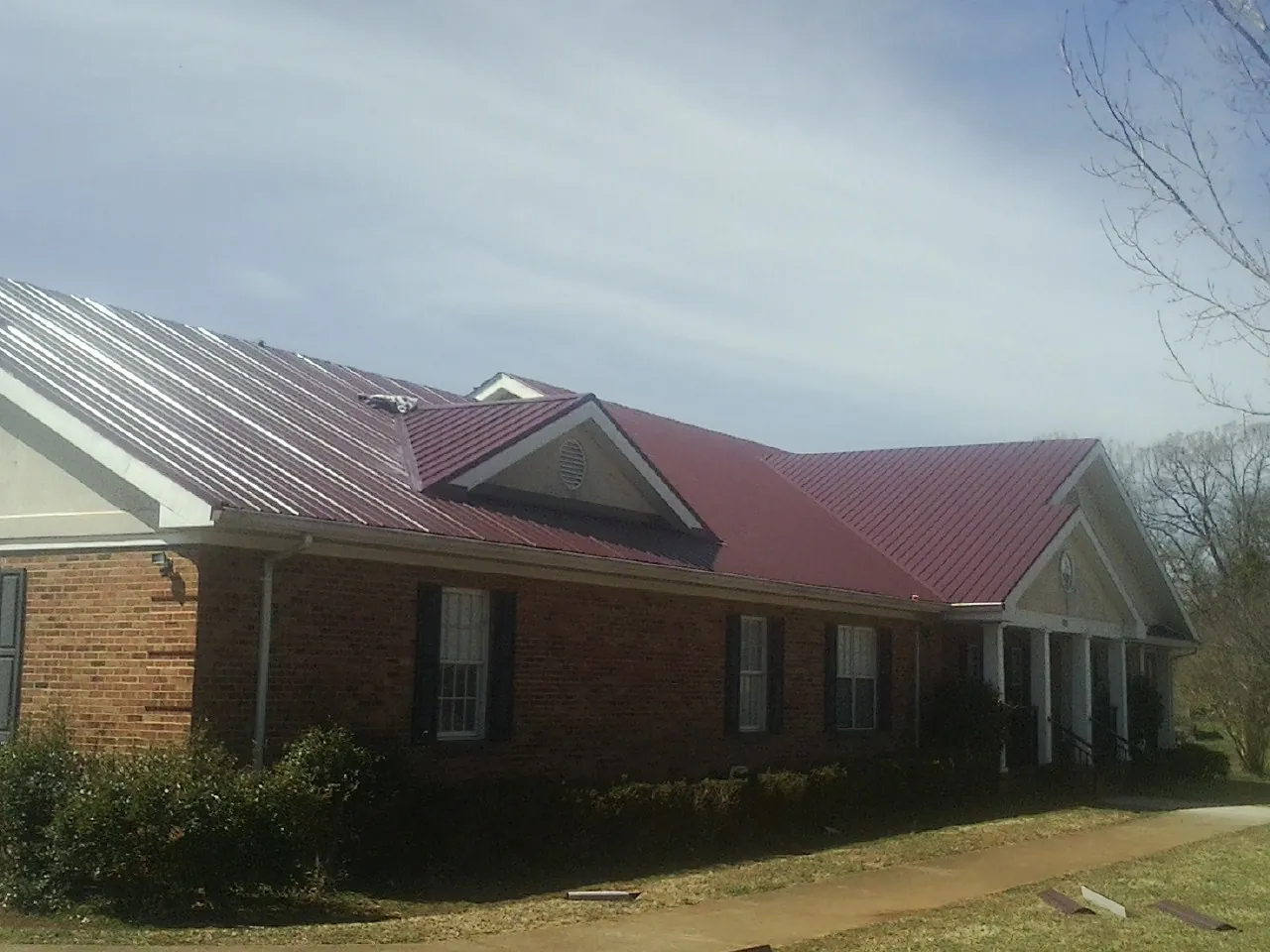 Red metal roof with gabled entries on a long brick building, from a Hail Damage Roof Repair job in Red Cloud