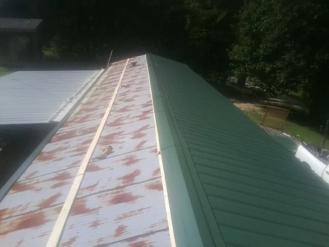Old rusted panels beside newly installed green metal roofing — Wind Damage Roof Repair by Roofing Brothers in Red Cloud