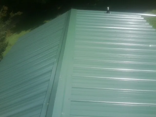 New green metal panels meeting at the ridge of a roof — Flat Roof Repair work by our crew in Red Cloud