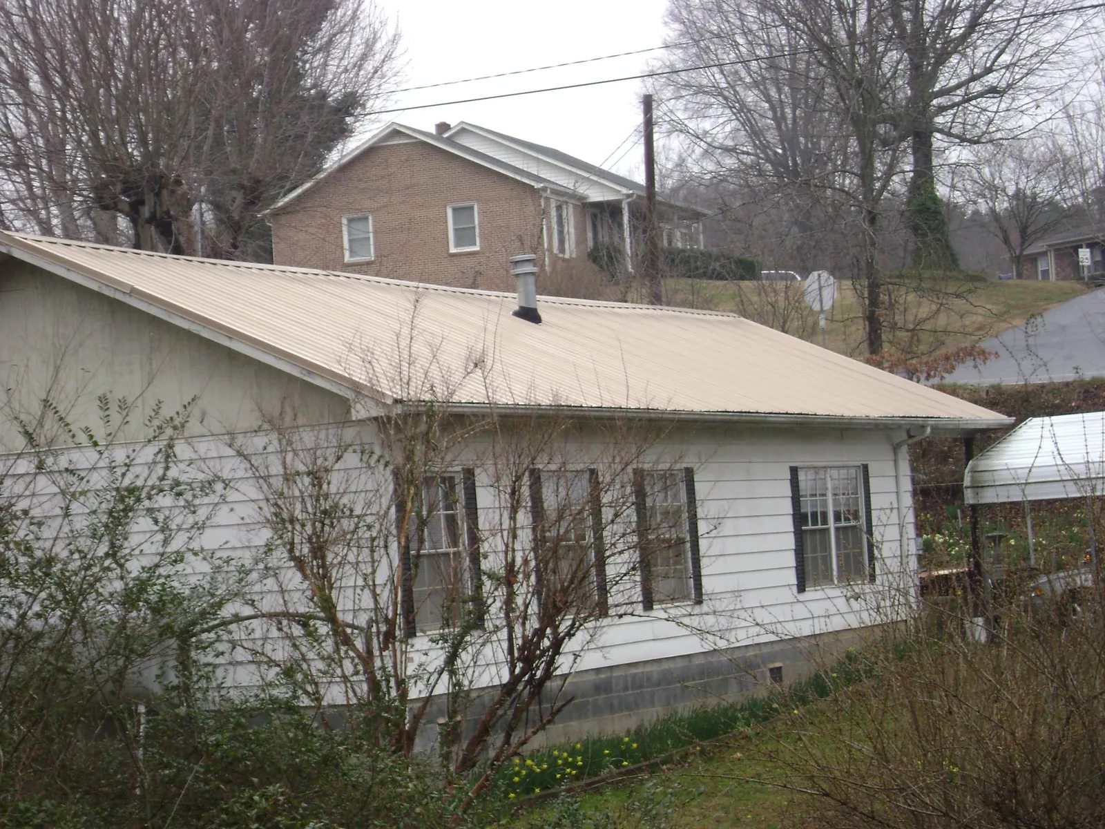 Tan metal roof on a white sided house set into a hillside — Commercial Roofing by Roofing Brothers in Red Cloud
