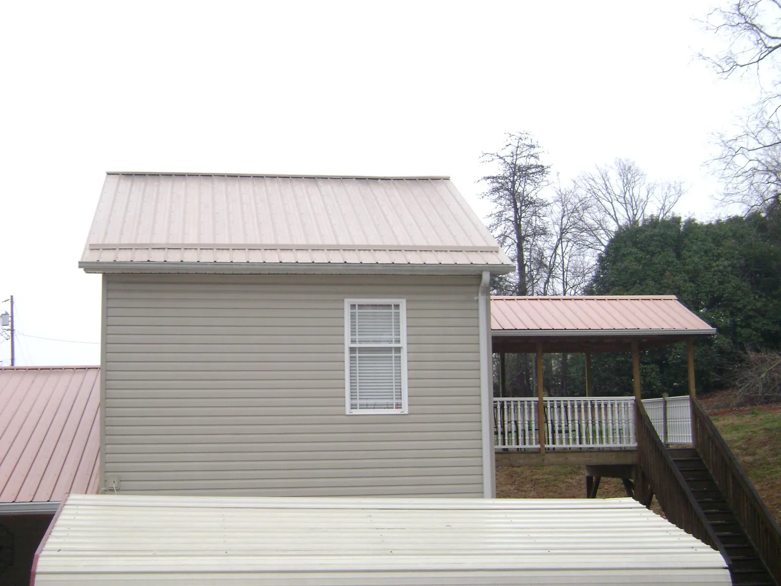 Tan metal roofs on a two story addition and attached porch, from a Roof Replacement job in Red Cloud